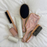 Bamboo Paddle Brush in Pink Chantilly with assorted styling tools and hair care