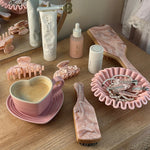 Bamboo Paddle Brush in Pink Chantilly on dresser with assorted hair care, accessories, and coffee